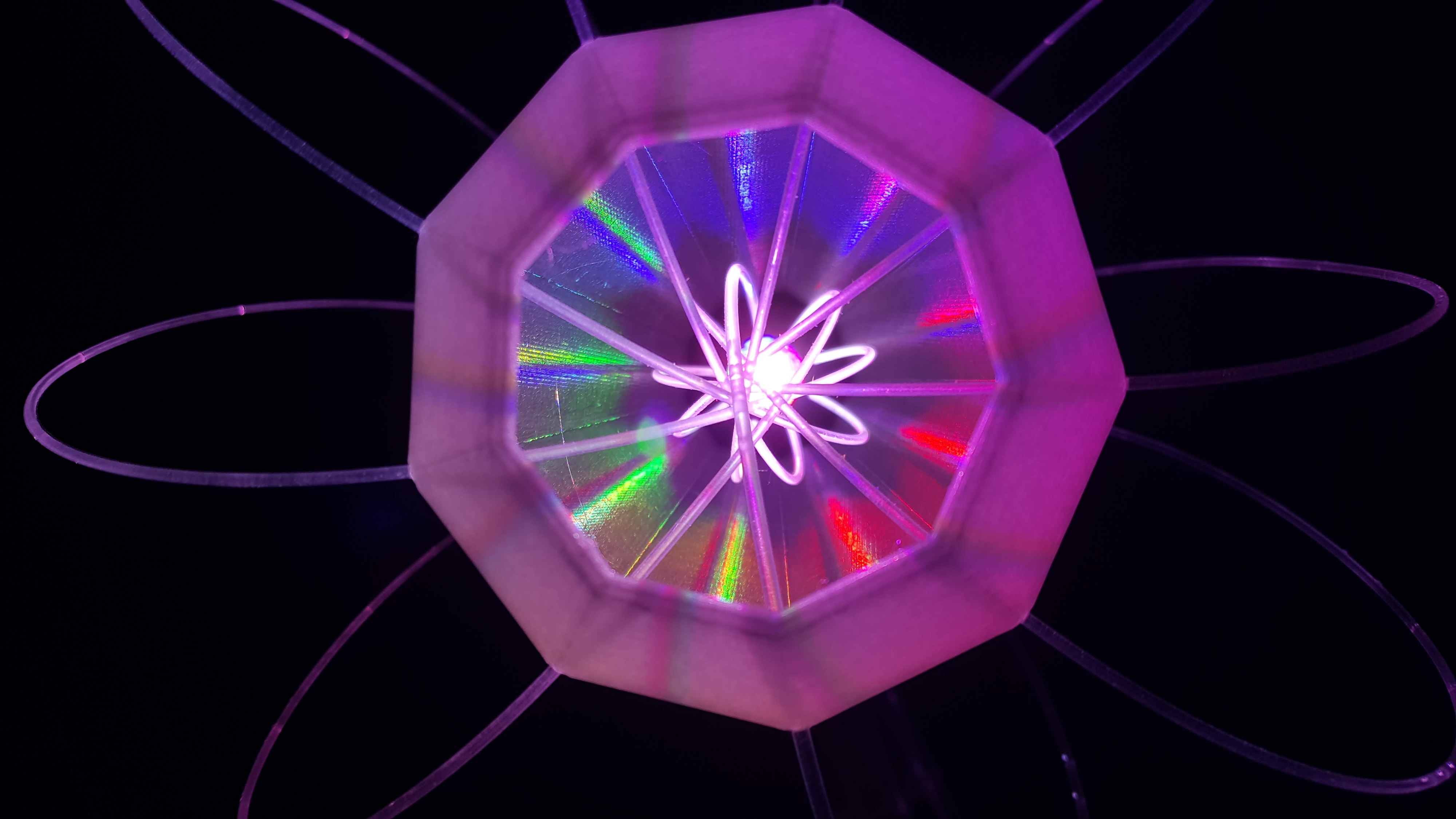 IXFID — fialová geometrická světelná socha ve tvaru atomového květu na černém pozadí