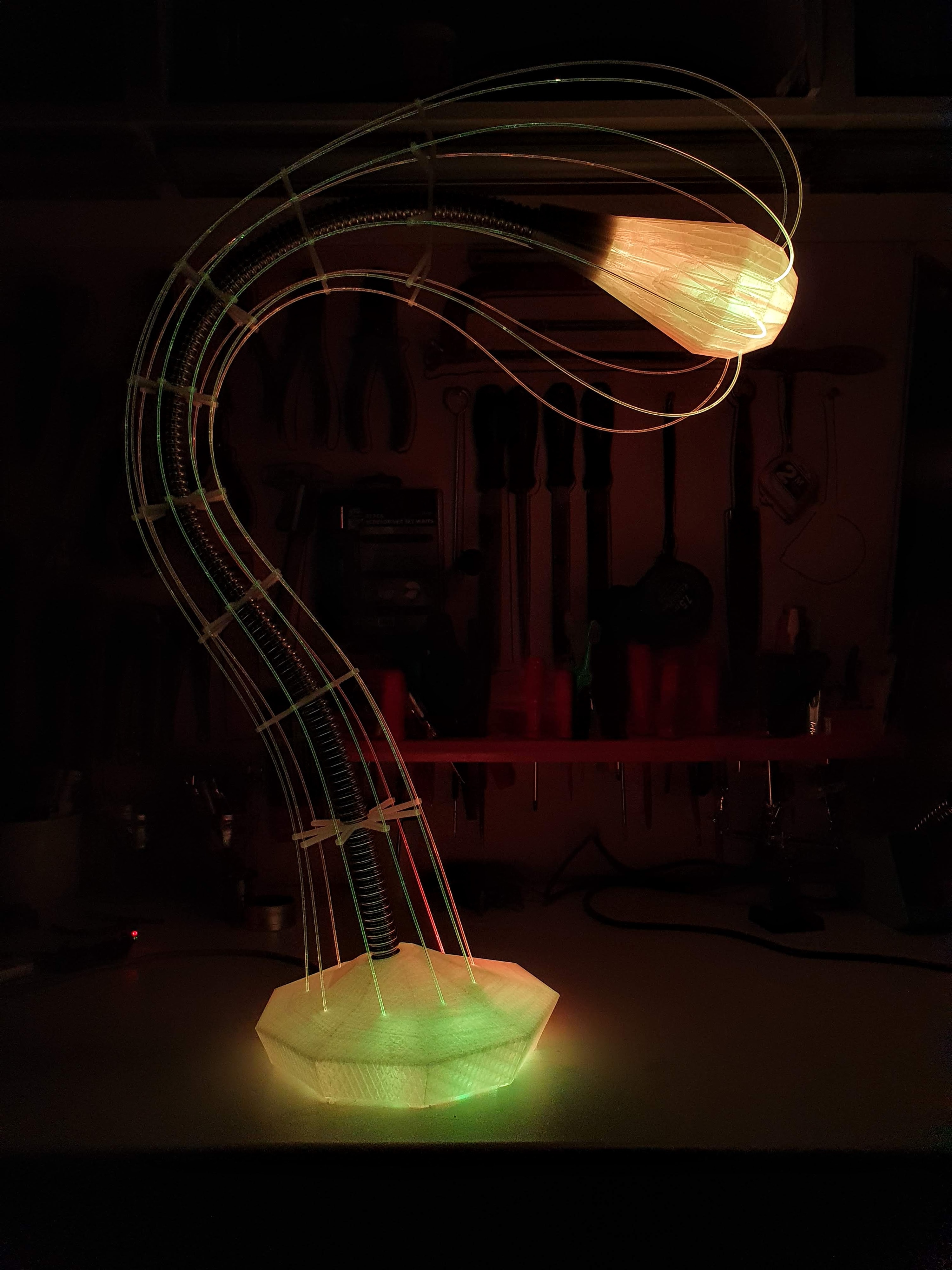 IXFID — 3D tištěná zakřivená lampa se zeleným podstavcem a oranžovou hlavou v tmavé dílně